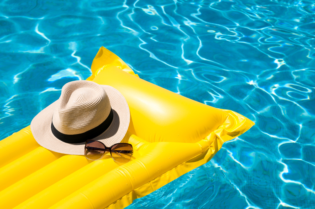 chapeau de paille et lunettes de soleil posées sur un matelas gonflable jaune dans une piscine